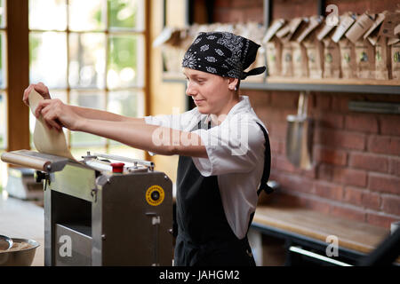 Woman cooks dough on machine for making pasta Stock Photo