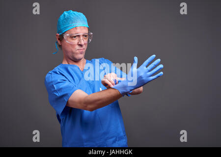A middle aged male doctor in blue scrubs taking his gloves on and getting ready Stock Photo