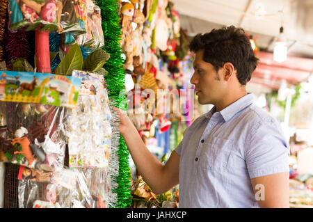 QUITO, ECUADOR- 07 MAY, 2017: Handsome young man watching beautiful and colorful christmas tree decoration in a market