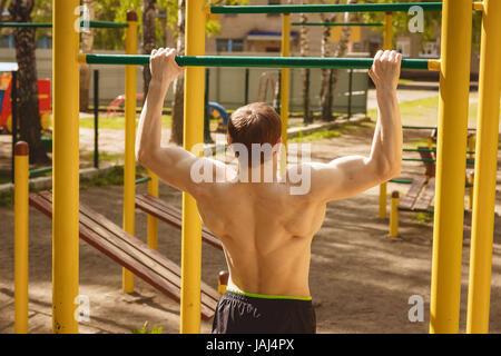 young man doing pull ups on horizontal bar outdoors Stock Photo