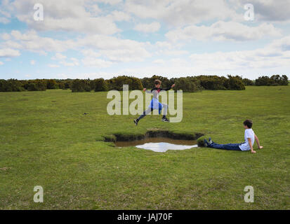 Young boys play jumping over puddles in the New Forest Stock Photo