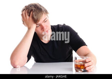 Junger Mann mit kurzen blonden Haaren und einem schwarzen T-Shirt sitzt an einem Tisch und hält Glas mit Branntwein in der Hand, isoliert vor weißem Hintergrund. Stock Photo