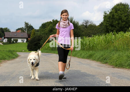 Ein Mädchen geht mit einem Hund Gassi auf einem Weg Stock Photo