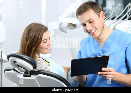 Happy dentist and patient commenting treatments in a tablet application in a consultation with medical equipment in the background Stock Photo