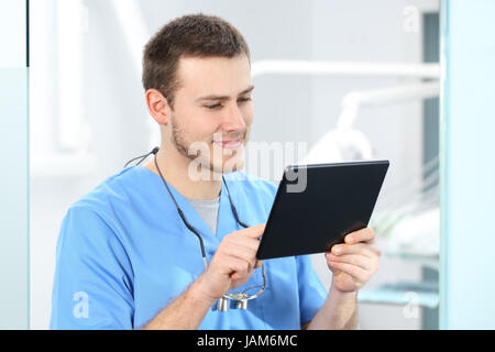 Doctor wearing blue coat working on line with a tablet in a dentist office Stock Photo