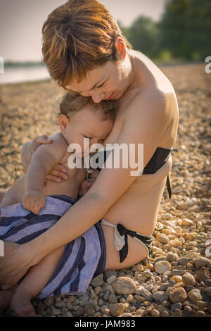 Mother hugging her baby son on the beach in late afternoon sun Stock Photo