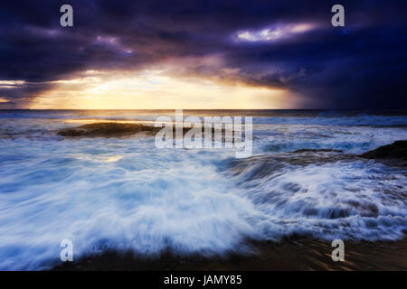 Dark sunrise over sea horizon from Bungan Beach on Sydney Pacific Coast. Bright rising sun penetrates thick clouds in stormy weather, reflecting from  Stock Photo
