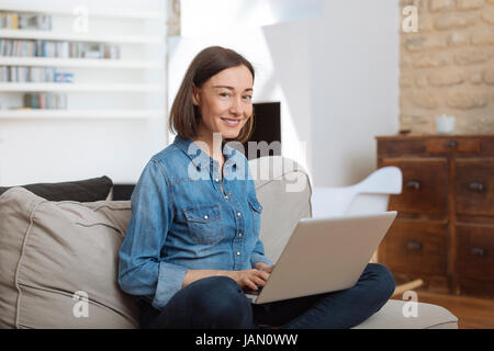 Attractive mature woman using a laptop while relaxing on a sofa at home Stock Photo