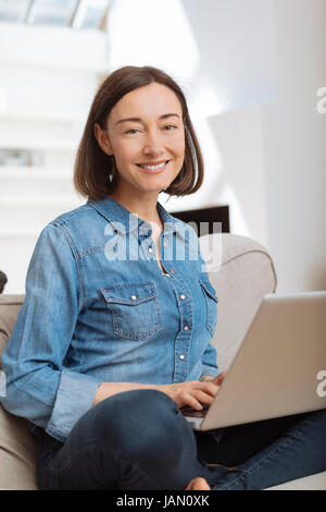 Attractive mature woman using a laptop while relaxing on a sofa at home Stock Photo