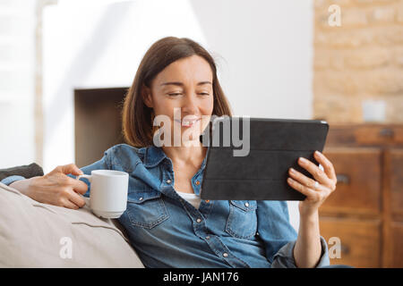 Mature woman using tablet computer while relaxing on sofa at home Stock Photo