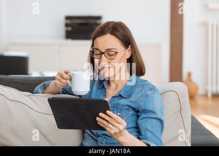 Mature woman using tablet computer while relaxing on sofa at home Stock Photo