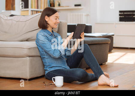 Mature woman using tablet computer while relaxing on sofa at home Stock Photo