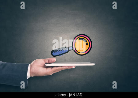 Businessman hand holding digital tablet with magnifying glass icon on blackboard Stock Photo
