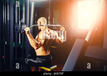 very power athletic guy bodybuilder, execute exercise with gym apparatus, on broadest muscle of back Stock Photo