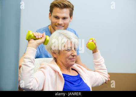 physiotherapist assisting senior woman to lift dumbbells Stock Photo
