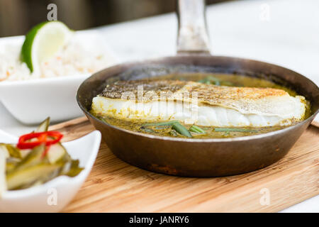 Sauteed cod in green sauce, cooked in a pan and over a wooden board, in a garden ready to be  served. Stock Photo