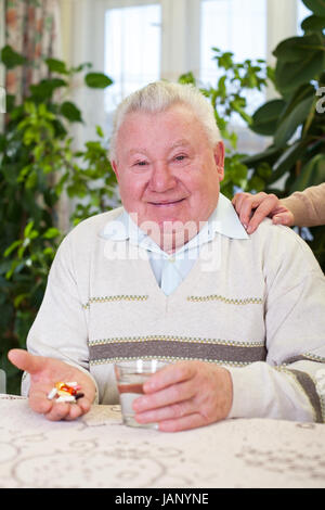 Picture of an elderly man holding his pills and a glass of water Stock Photo