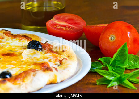 detail of a pizza on a wooden table with ingredients all around Stock Photo