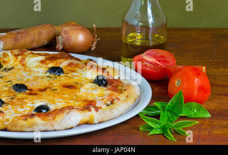 detail of a pizza on a wooden table with ingredients all around Stock Photo