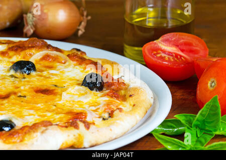 detail of a pizza on a wooden table with ingredients all around Stock Photo