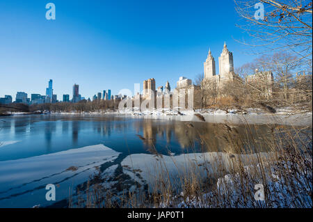 Scenic view of the Upper West Side skyline reflecting in the ice of the frozen Central Park lake after a winter snow storm in New York City Stock Photo