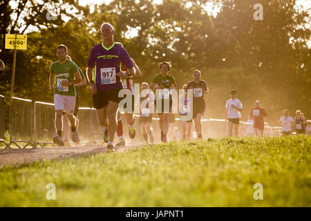 Male adn female runners taking part in a10K run as the sunaets behind them, backlighting the dust rising from the track theay are running on. Stock Photo