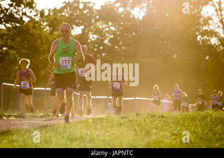 Male adn female runners taking part in a10K run as the sunaets behind them, backlighting the dust rising from the track theay are running on. Stock Photo