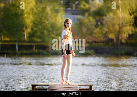Teenage girl in black shorts standing on pier over pond and looking back over shoulder Stock Photo