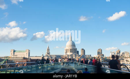 View of the Millennium bridge in London with St Paul cathedral and tourists and commuters walking