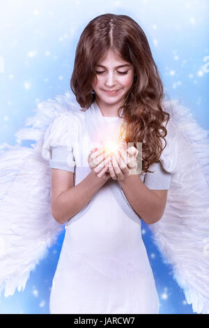 Cute Christmas angel on blue snowy background, adorable girl with candle in hands, religious winter holiday, peace and harmony concept Stock Photo