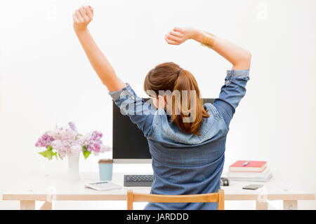 Woman stretching her arms sitting by the table at work next to computer Stock Photo