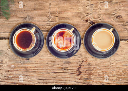 Three cups of coffee with black, white and flowing milk on wooden background Stock Photo