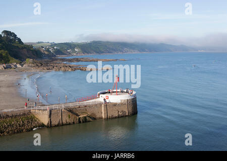 Sea mist rolls in from offshore across cliffs in South East Cornwall with the banjo pier of the seaside town of Looe, Cornwall in the foreground Stock Photo