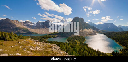 Mount Assiniboine, Sunburst Peak (foreground). in Mt.Assiniboine Provincial Park with Cerulean Lake, Sunburst Lake, Lake Magog, looking south from coordinates 50.908012,-115.627871, midday in summer, sunrays creeping in, panorama Stock Photo