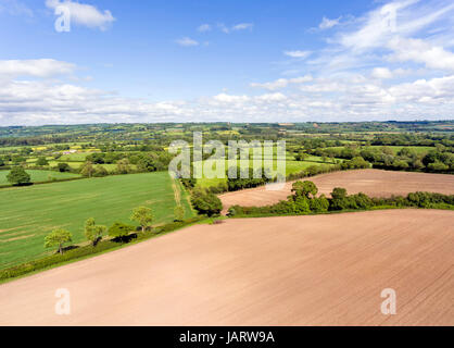 Aerial view of farm fields with ploughed brown fields, green pastures, meadows, in an English, summer countryside . Stock Photo