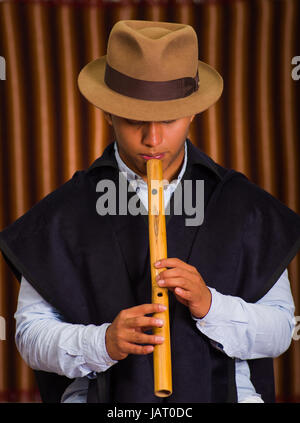 Close up portrait of indigenous young man wearing hat and poncho playing the quena flute Stock Photo