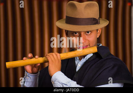 Close up portrait of indigenous young man wearing hat and poncho playing the quena flute Stock Photo