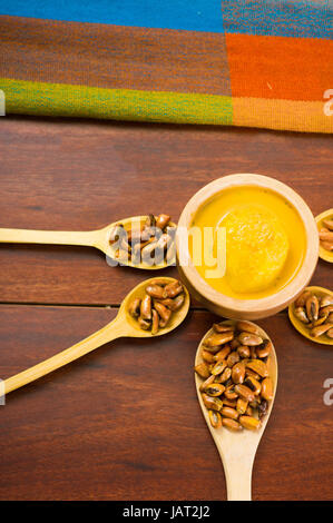 Wooden spoons with toasted corn grains, known as tostado in south america, spread around bowl containing yellow salsa, seen from above. Stock Photo