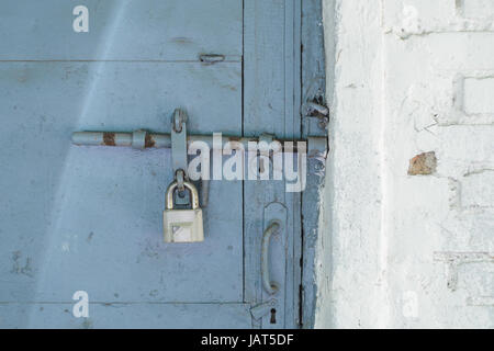 Padlock on the blue metal door. Locked on the castle is an old door in a white brick wall. Abstract background Stock Photo