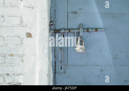 Padlock on the blue metal door. Locked on the castle is an old door in a white brick wall. Abstract background Stock Photo