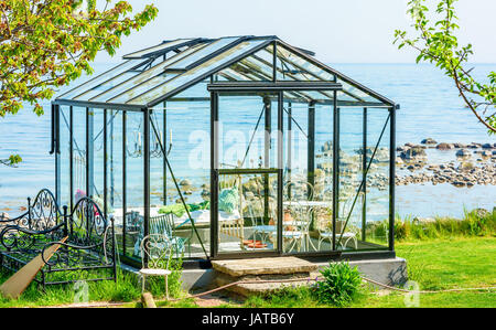 Simrishamn, Sweden - May 19, 2017: Environmental documentary.  Transparent living in this seaside greenhouse. Inside is a bed, a table and a chandelie Stock Photo