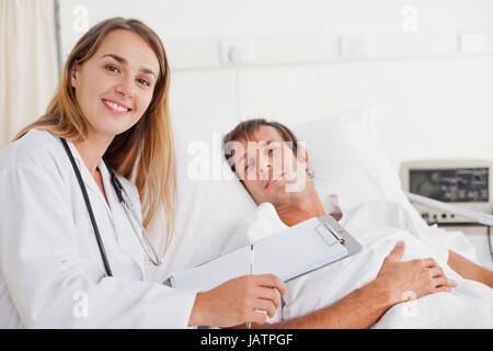 Smiling doctor looking at the camera while standing next to a hospital bed Stock Photo