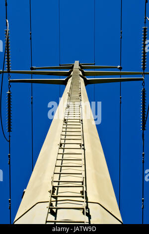 Looking up ladder on electrical tower with cables and insulators against blue sky. Stock Photo