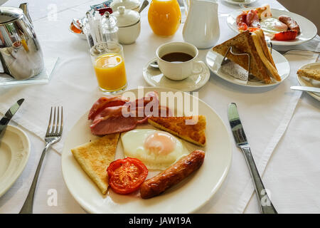 Ulster fry, full breakfast including fried egg, bacon rashers, tomato, sausage, soda bread and potato bread. Orange juice and coffee to drink. Stock Photo