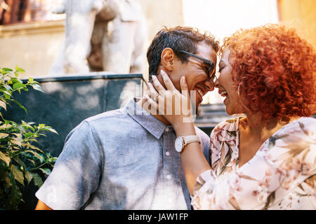 Cheerful young man and woman expressing love outdoors. Woman holding her partner close to her head and smiling. Stock Photo