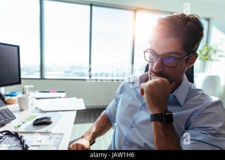 Closeup of  entrepreneur looking at the computer screen with concentration at his desk. Businessman wearing spectacles sitting in pensive mood  with h Stock Photo