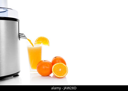 Juicing oranges. Fresh orange juice in glass next to silver juicer with fresh ripe oranges isolated on white background with reflection. Healthy fresh summer fruit. Stock Photo