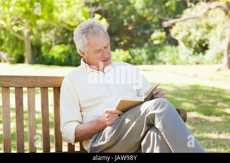 Man seriously reading a book as he sits on a bench Stock Photo