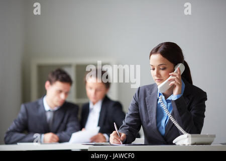 Portrait of smart businesswoman calling on the phone and making notes on background of working colleagues Stock Photo