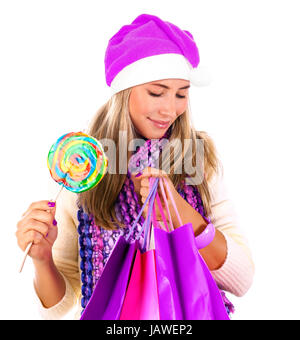 Portrait of cute woman with shopping bag and wearing Santa hat isolated on white background, holding in hands colorful lollipop, Christmastime concept Stock Photo